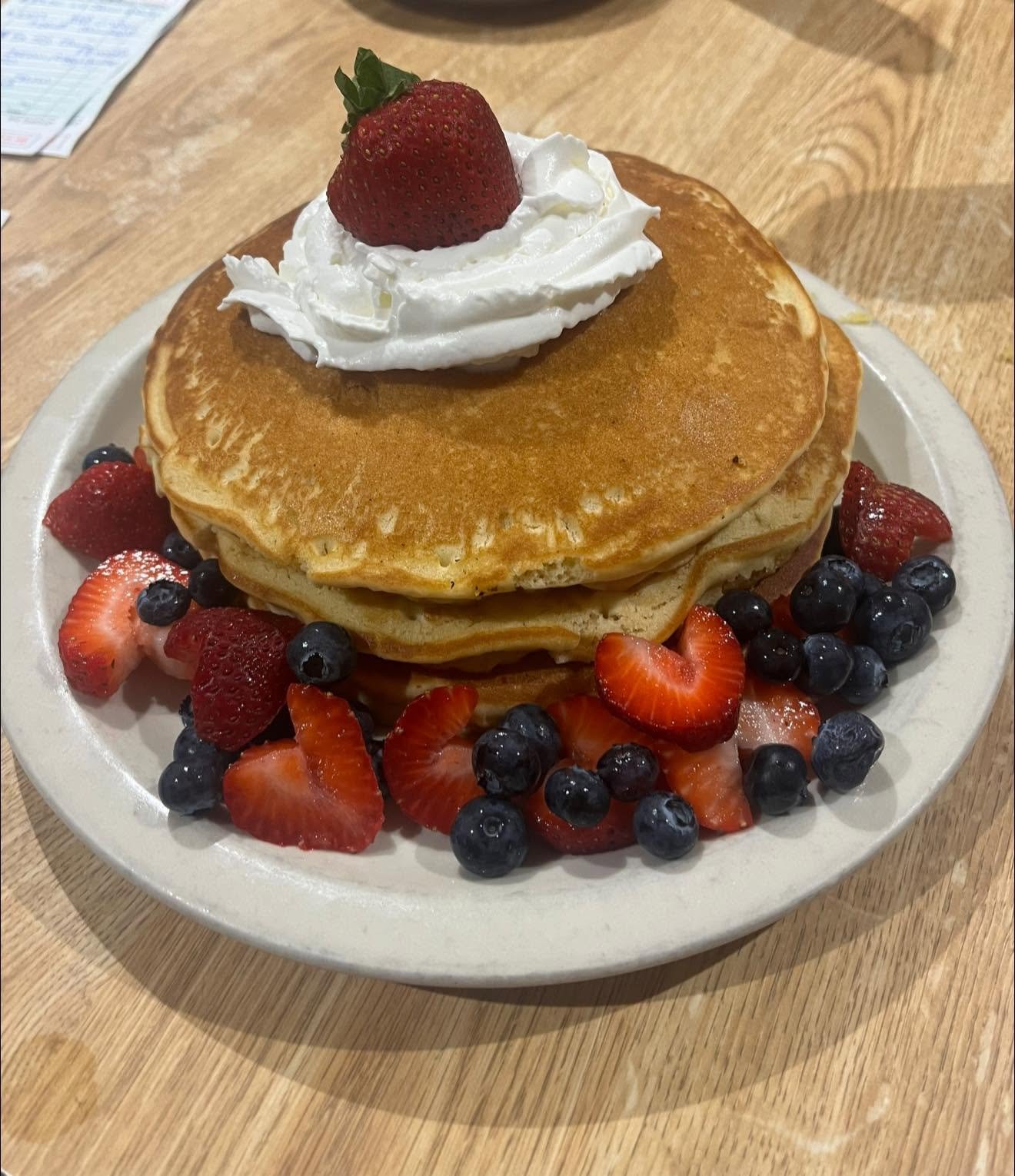 Stack of pancakes topped with whipped cream and berries
